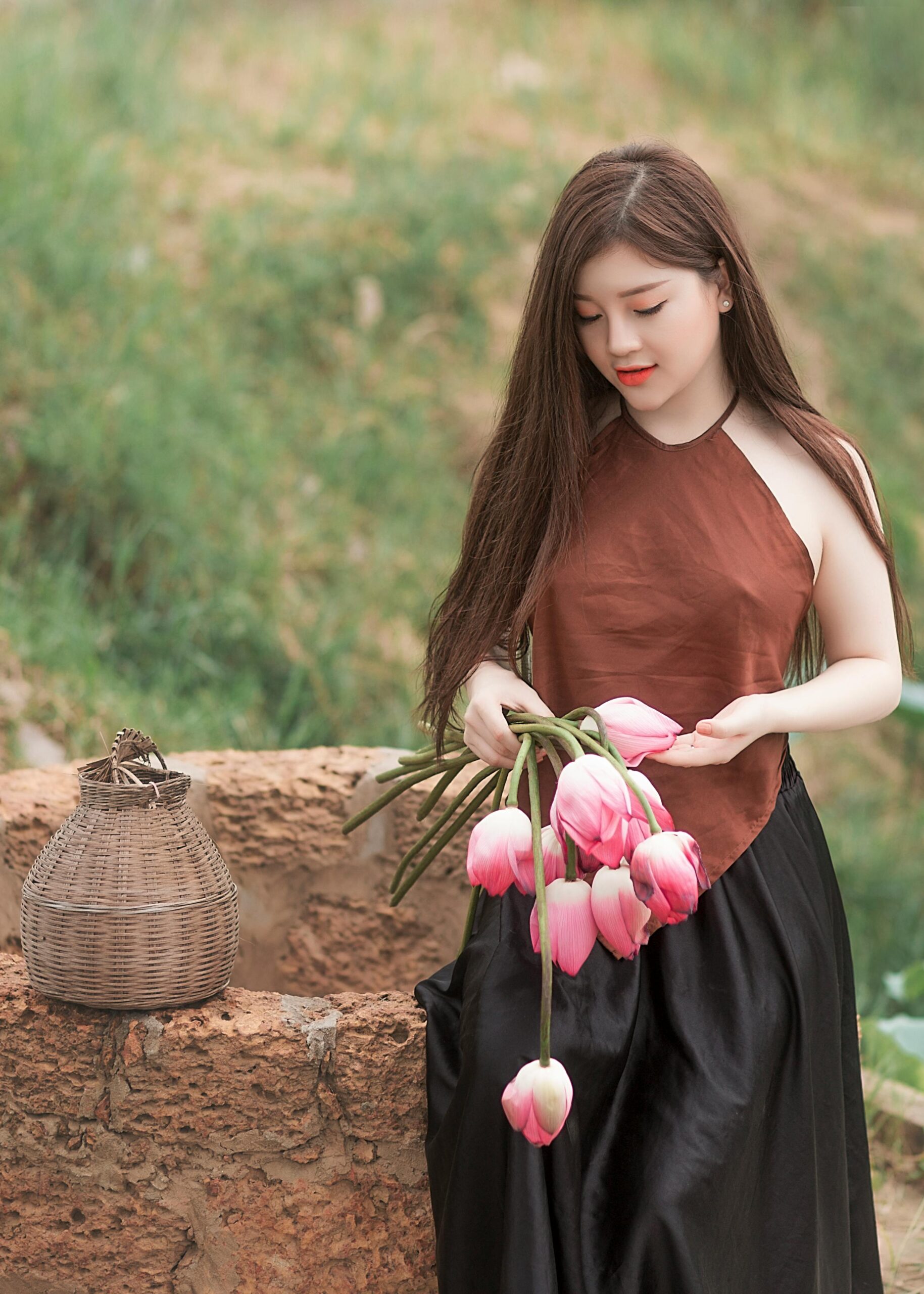 An elegant young woman holding pink tulips in a serene outdoor setting, embodying natural beauty and tranquility.